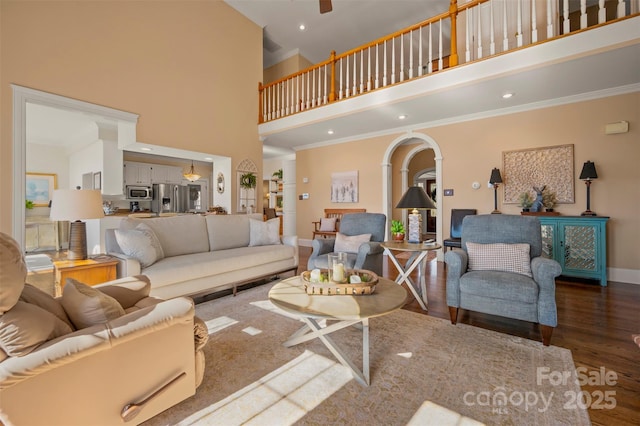 living room featuring crown molding, baseboards, wood finished floors, arched walkways, and a high ceiling