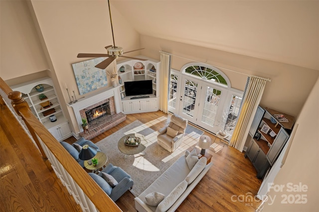 living room with a ceiling fan, high vaulted ceiling, a fireplace, and wood finished floors