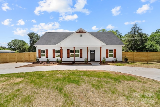 modern inspired farmhouse featuring a porch, fence, a shingled roof, and a front lawn