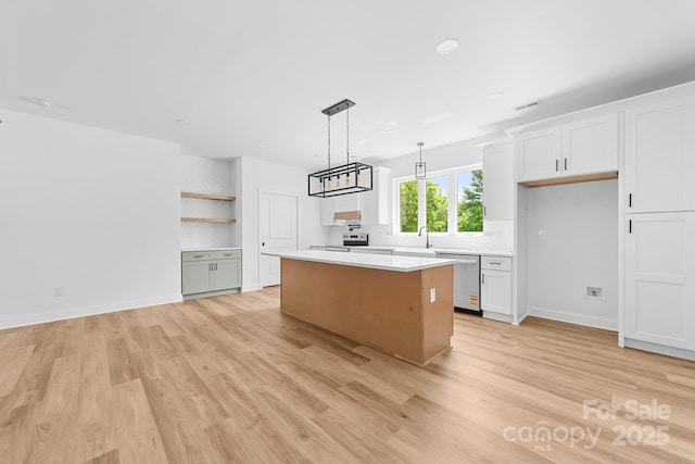 kitchen featuring a center island, stainless steel dishwasher, light countertops, light wood finished floors, and white cabinetry