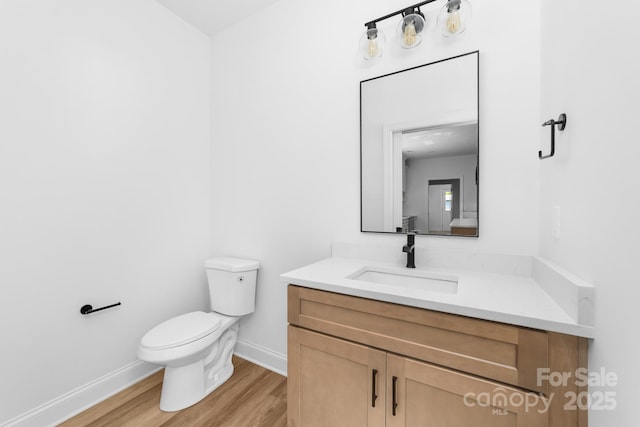 bathroom featuring toilet, baseboards, wood finished floors, and vanity