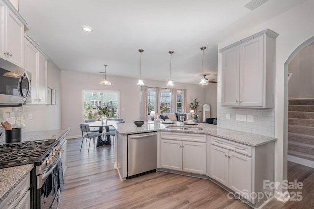 kitchen featuring stainless steel appliances, a sink, arched walkways, ceiling fan, and a peninsula