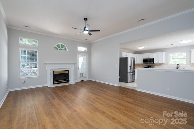 unfurnished living room with a ceiling fan, wood finished floors, a premium fireplace, and visible vents