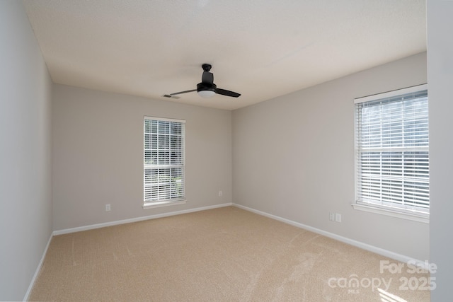 carpeted empty room with a ceiling fan, visible vents, baseboards, and a wealth of natural light