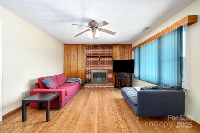 living room with a ceiling fan, a brick fireplace, light wood-style floors, and visible vents