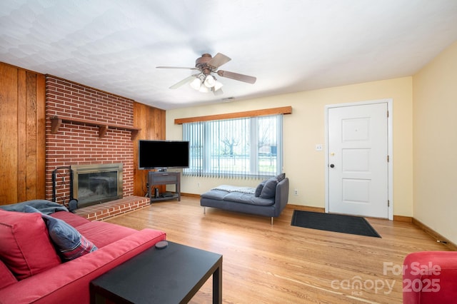 living area with a brick fireplace, wooden walls, ceiling fan, and wood finished floors