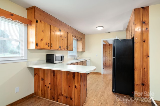kitchen with light countertops, stainless steel microwave, a sink, freestanding refrigerator, and a peninsula