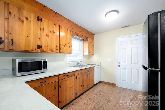 kitchen with light countertops, a sink, freestanding refrigerator, dishwasher, and stainless steel microwave