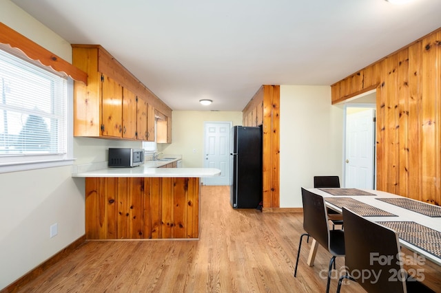kitchen featuring light countertops, stainless steel microwave, light wood finished floors, freestanding refrigerator, and a peninsula