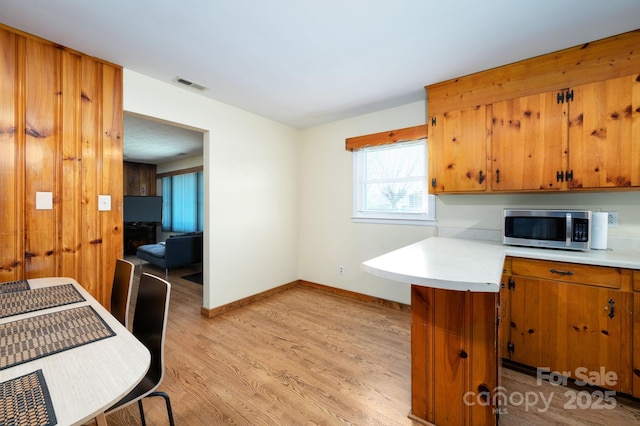 kitchen featuring light countertops, visible vents, light wood finished floors, stainless steel microwave, and brown cabinets
