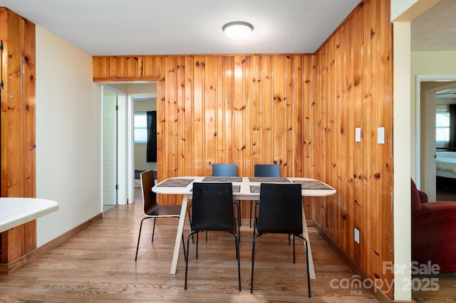 dining space featuring baseboards, wood walls, a healthy amount of sunlight, and wood finished floors