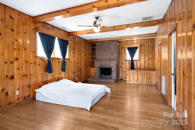 bedroom featuring visible vents, wooden walls, beamed ceiling, and wood finished floors
