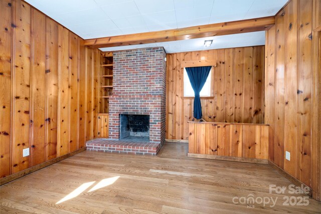 unfurnished living room with beamed ceiling, a fireplace, wood finished floors, and wood walls