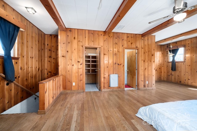 bedroom featuring wood finished floors, wooden walls, beamed ceiling, and radiator