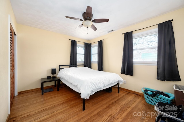 bedroom featuring light wood-type flooring, baseboards, ceiling fan, visible vents, and a closet