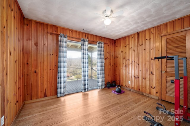 workout room featuring baseboards, wooden walls, ceiling fan, and wood finished floors