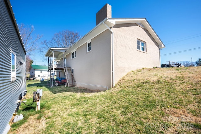 view of side of property featuring a lawn, a chimney, stairs, and brick siding