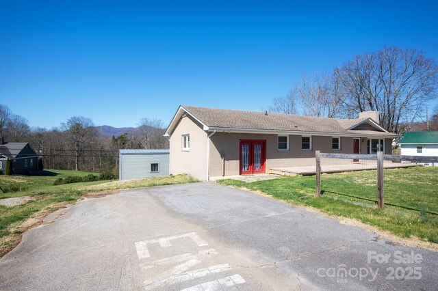 ranch-style home featuring french doors, an outdoor structure, brick siding, fence, and a front lawn