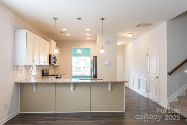 kitchen with a kitchen bar, visible vents, stainless steel appliances, and a peninsula