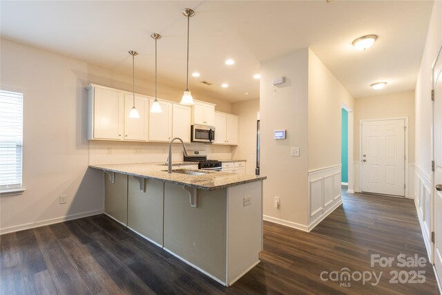kitchen featuring dark wood-style flooring, stainless steel appliances, light stone countertops, a breakfast bar, and a peninsula