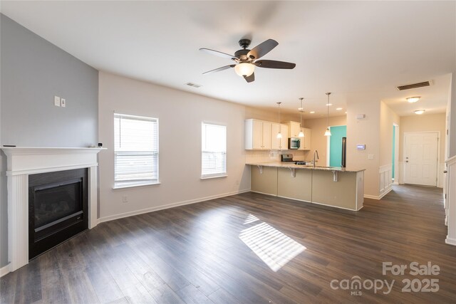 unfurnished living room with dark wood-style flooring, a sink, ceiling fan, and visible vents
