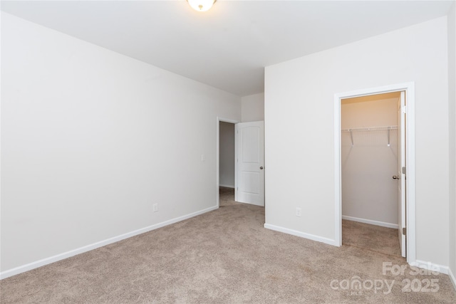 unfurnished bedroom featuring light colored carpet, a closet, baseboards, and a spacious closet