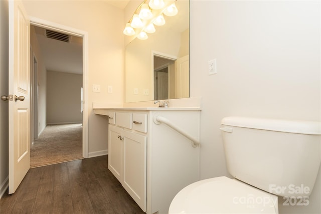 half bathroom featuring wood finished floors, vanity, toilet, and visible vents