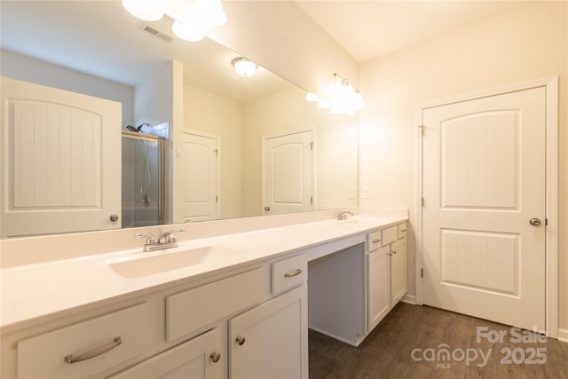 full bath with visible vents, walk in shower, double vanity, wood finished floors, and a sink