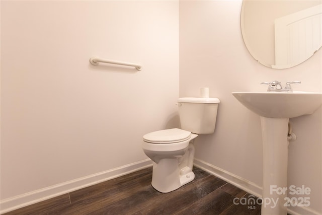 half bath with toilet, a sink, baseboards, and wood finished floors