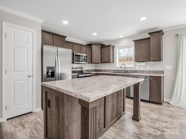 kitchen with a sink, ornamental molding, appliances with stainless steel finishes, and dark brown cabinets
