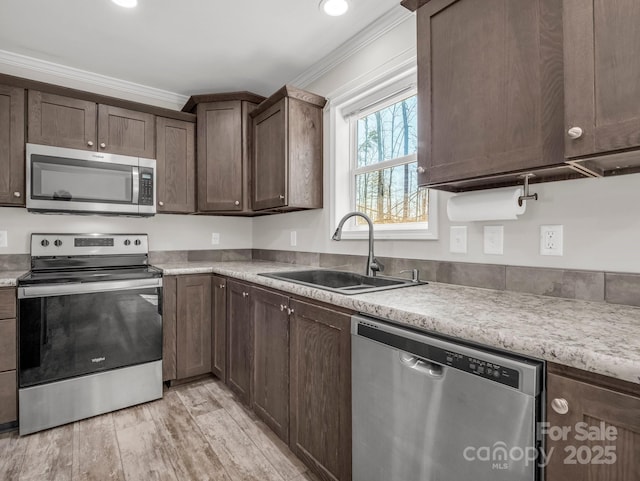 kitchen featuring crown molding, dark brown cabinets, appliances with stainless steel finishes, a sink, and light wood-style floors
