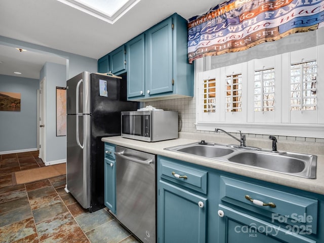 kitchen featuring light countertops, appliances with stainless steel finishes, a sink, blue cabinets, and backsplash