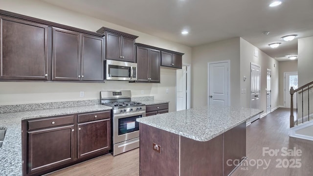 kitchen featuring light stone countertops, appliances with stainless steel finishes, dark brown cabinetry, light wood-style floors, and a center island
