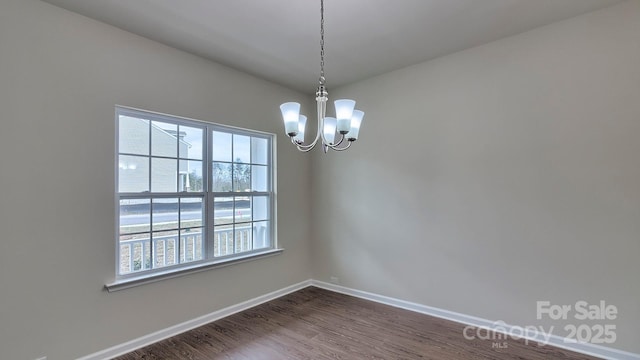 unfurnished room featuring baseboards, a notable chandelier, and dark wood-style flooring