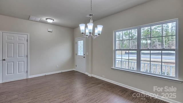 empty room featuring dark wood-type flooring, a healthy amount of sunlight, a chandelier, and baseboards