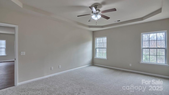 unfurnished room featuring a tray ceiling, visible vents, ceiling fan, and plenty of natural light