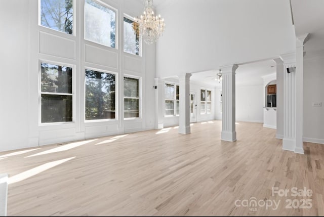 15009 Lisha Ln, Charlotte, NC 28277 - unfurnished living room featuring baseboards, ceiling fan with notable chandelier, light wood-style floors, a towering ceiling, and ornate columns