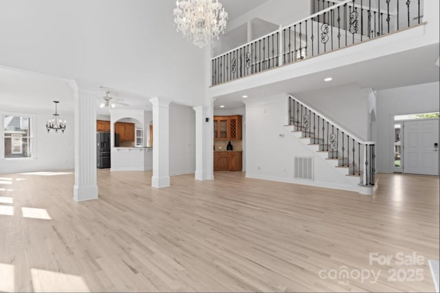 15009 Lisha Ln, Charlotte, NC 28277 - unfurnished living room featuring stairway, ornate columns, ceiling fan with notable chandelier, visible vents, and light wood-style flooring