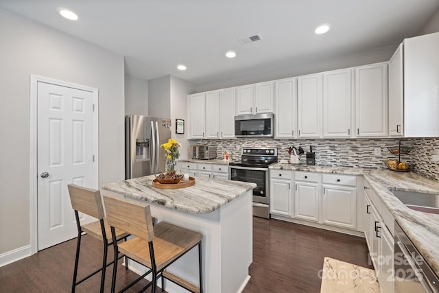 kitchen featuring a breakfast bar area, light stone countertops, appliances with stainless steel finishes, white cabinets, and dark wood-style flooring
