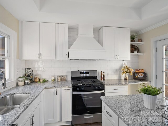 kitchen featuring a tray ceiling, a sink, open shelves, premium range hood, and stainless steel range with gas stovetop