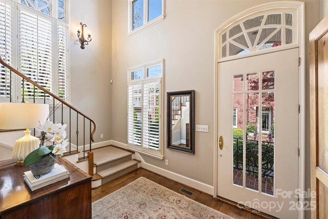 foyer entrance featuring stairs, wood finished floors, baseboards, visible vents, and a towering ceiling