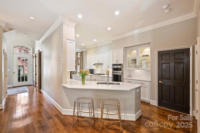 kitchen featuring light countertops, a sink, appliances with stainless steel finishes, a peninsula, and glass insert cabinets