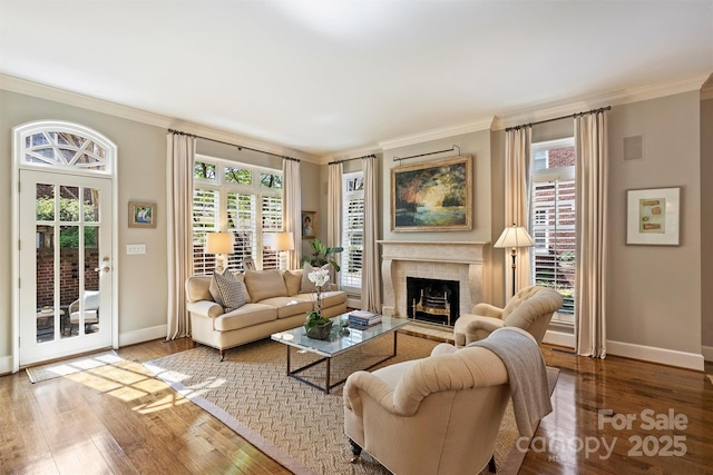 living area featuring baseboards, a fireplace with raised hearth, wood finished floors, and crown molding