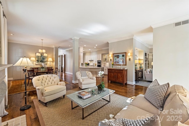 living area featuring a notable chandelier, dark wood-style flooring, baseboards, visible vents, and ornate columns