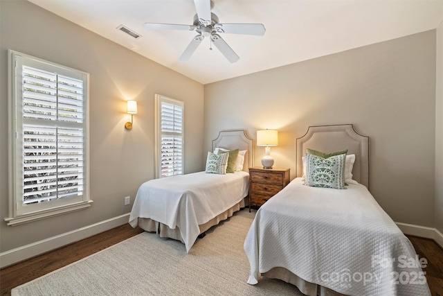 bedroom with a ceiling fan, visible vents, baseboards, and wood finished floors