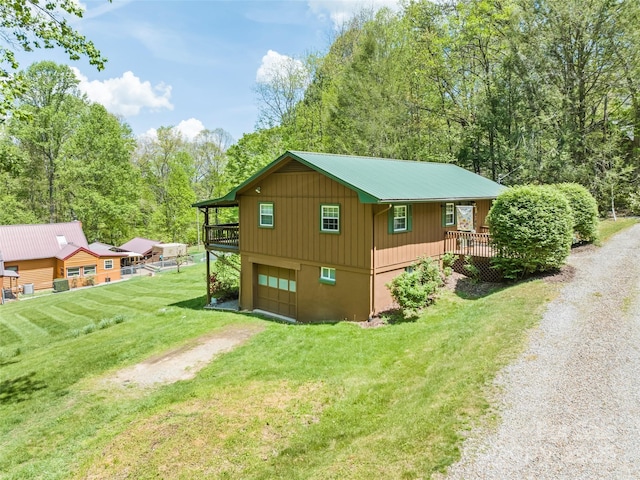 view of side of home with driveway, metal roof, a wooden deck, a garage, and a yard