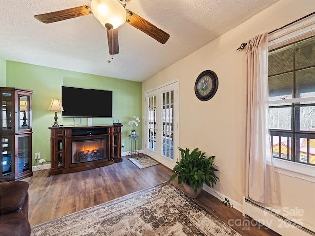 living area with baseboard heating, a textured ceiling, a glass covered fireplace, french doors, and wood finished floors