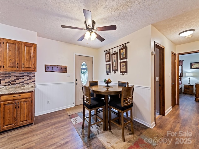 dining area with a ceiling fan, a textured ceiling, wainscoting, and wood finished floors