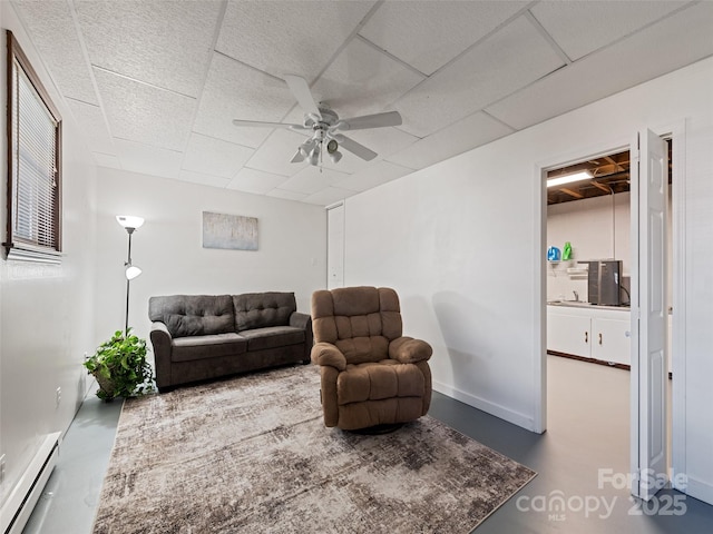 living area with a baseboard radiator, concrete floors, a ceiling fan, and a paneled ceiling