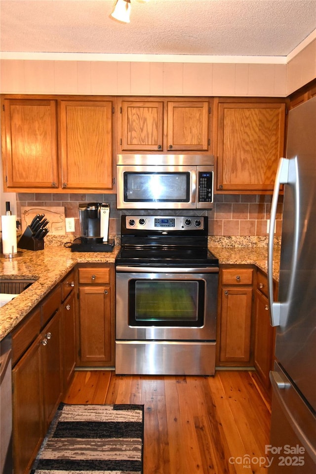 301 Pinnacle Inn Rd Unit 3219, Beech Mountain, NC 28604 - kitchen featuring appliances with stainless steel finishes, light wood-type flooring, brown cabinetry, tasteful backsplash, and a textured ceiling